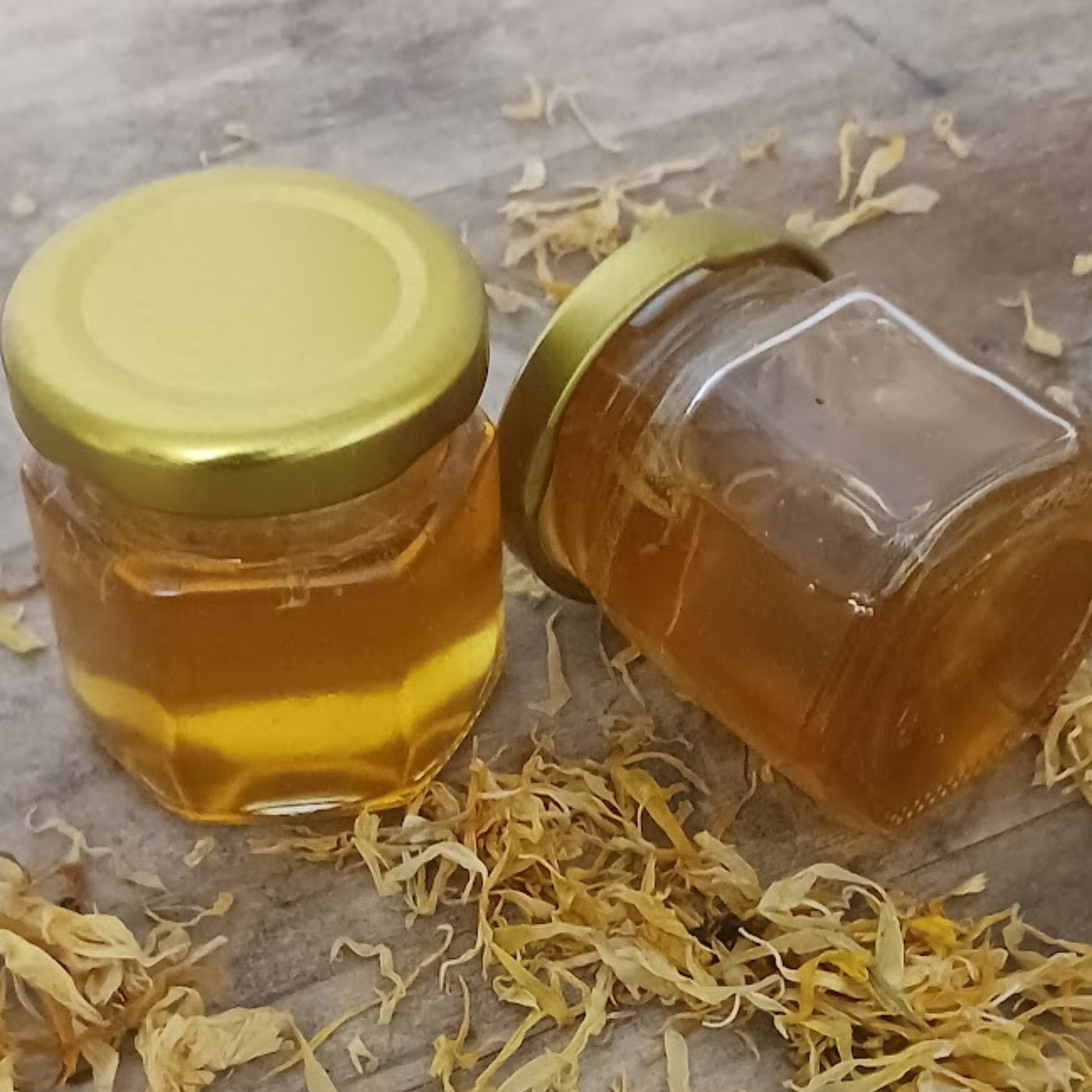 Calendula Glow Honey 2oz jars with scattered calendula petals on rustic wood surface