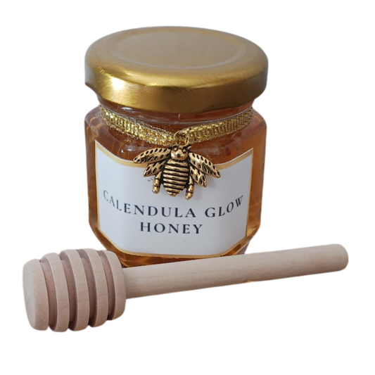 Calendula Glow Honey in hexagonal jar with gold lid, ribbon, bee charm and wooden honey dipper