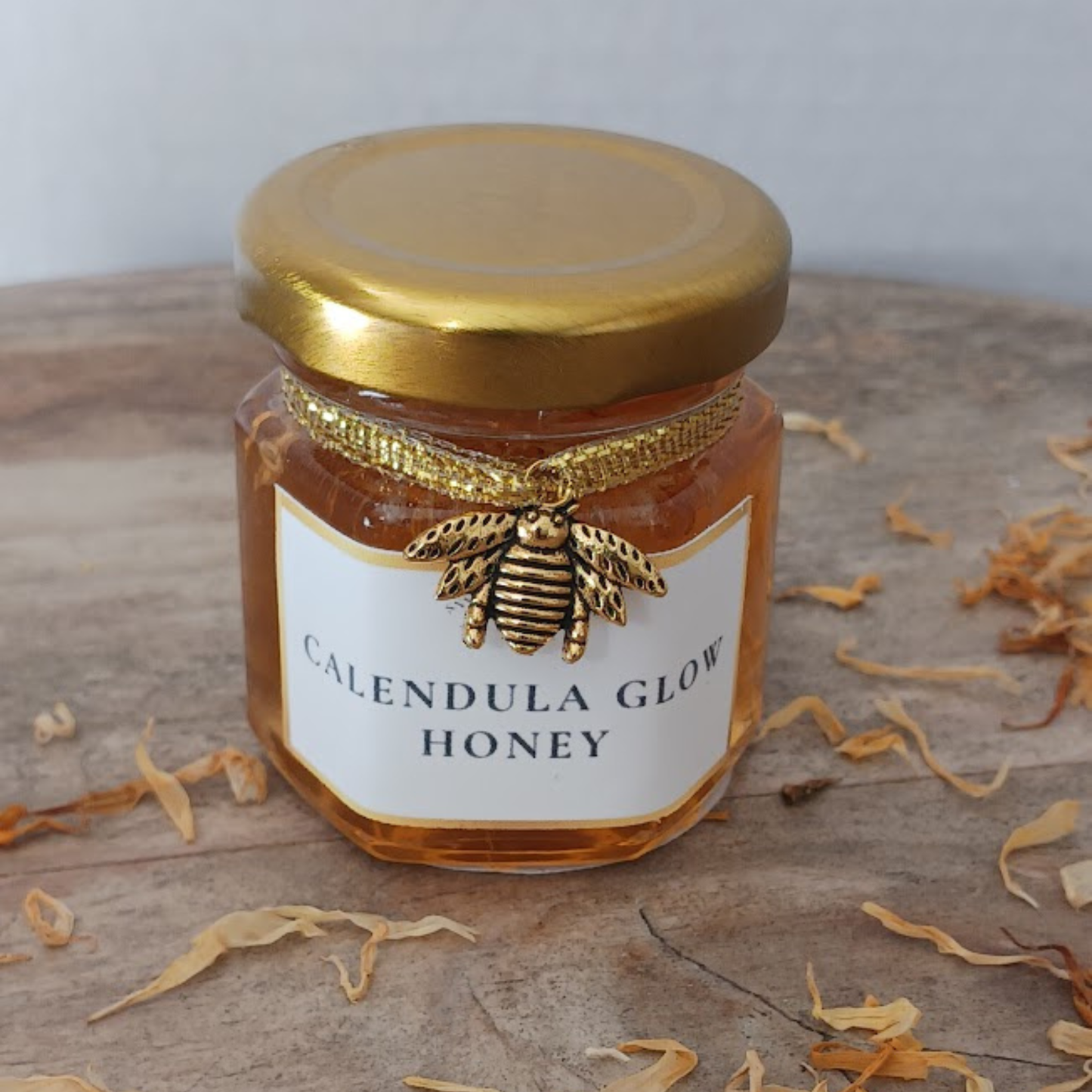 Calendula Glow Honey 2oz hexagonal jar with gold lid and bee charm on rustic wood